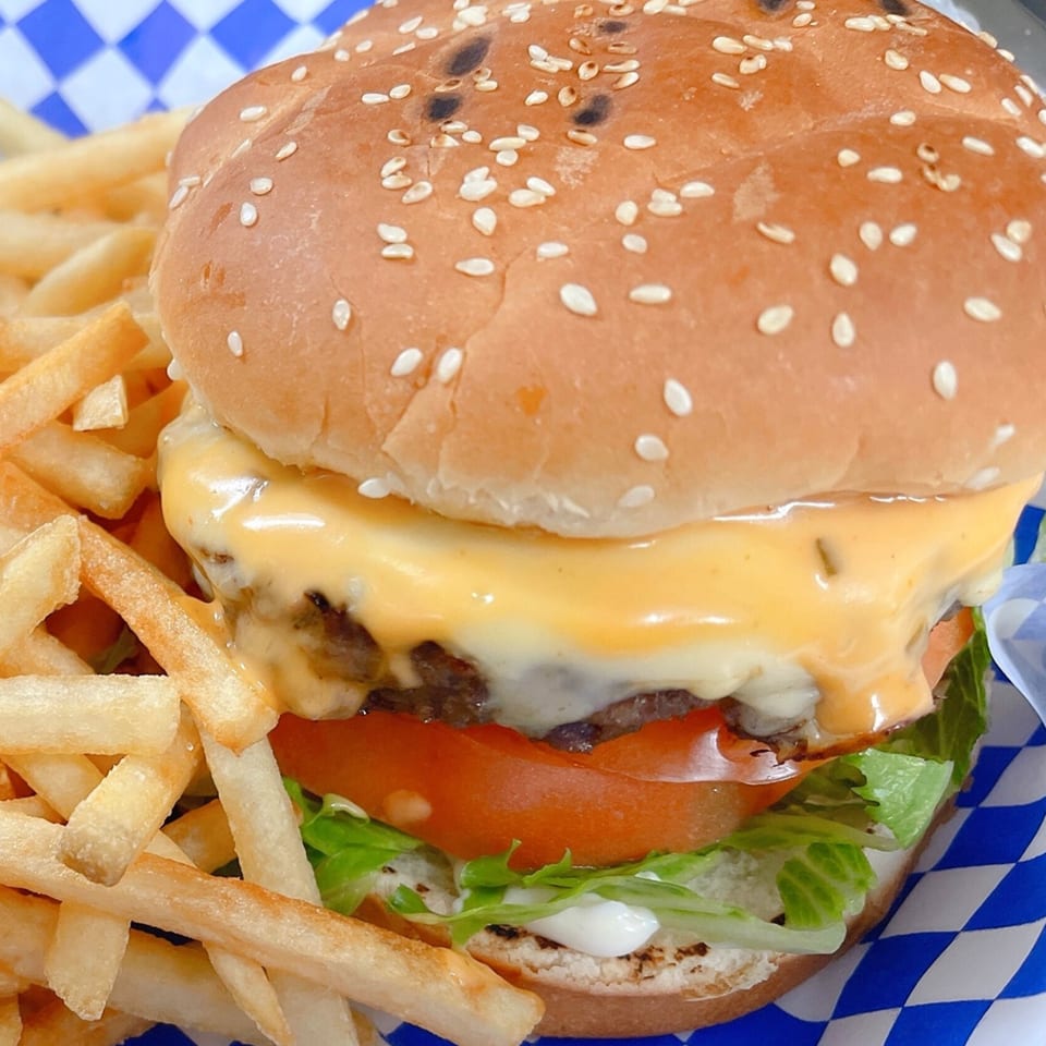 Cheeseburger with melted cheese, lettuce, tomato, and fries in a blue and white checkered basket.