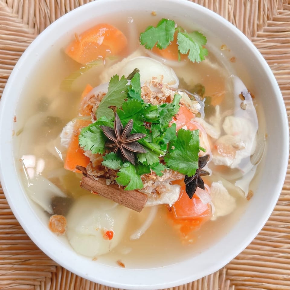 Close-up of Thai soup with carrots, cilantro, star anise, and cinnamon stick in a white bowl.