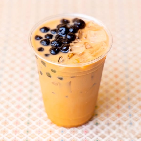A Thai iced tea with boba and ice in a clear plastic cup on a patterned tablecloth.