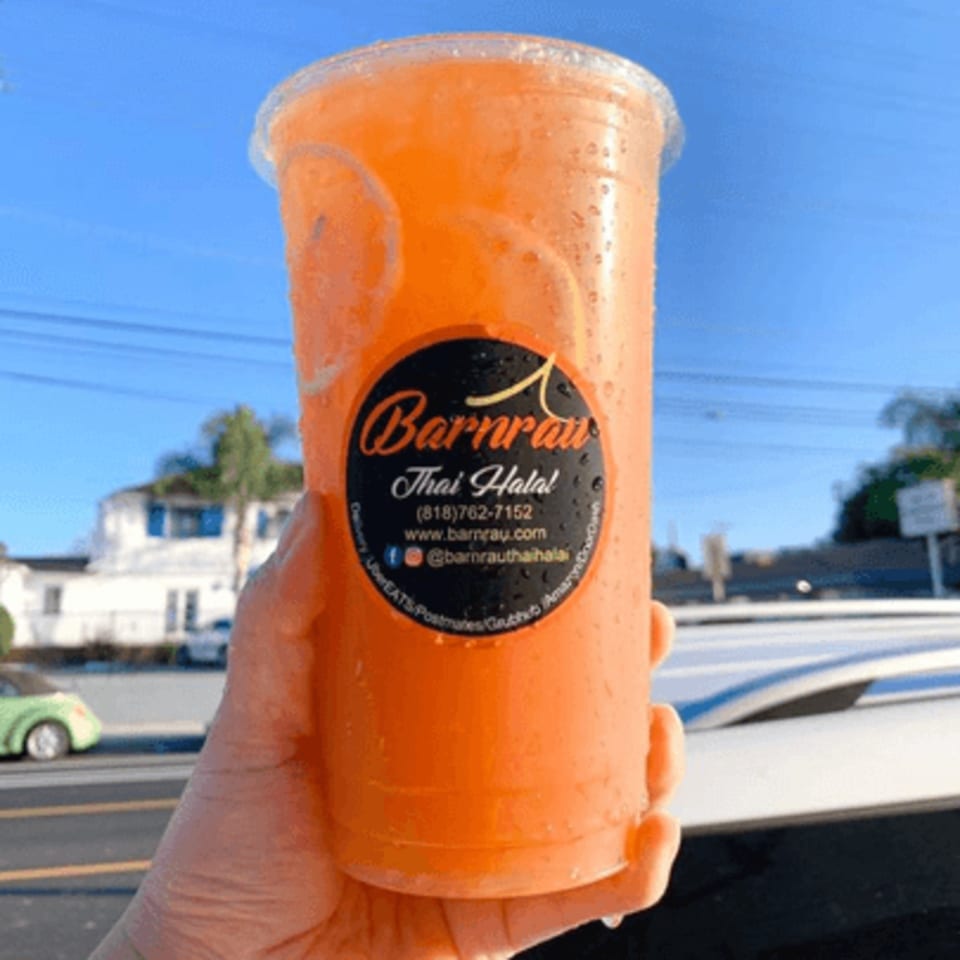 Hand holding a large plastic cup of Barnrau Thai Halal Cuisine's orange drink with citrus slices.
