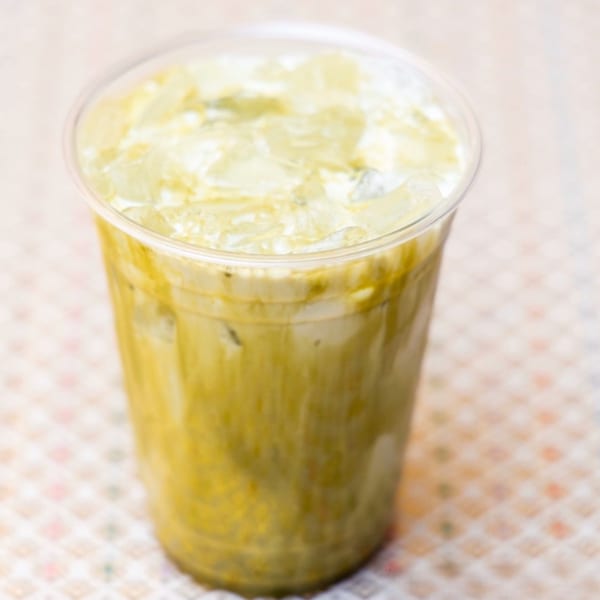 Iced green tea latte with a creamy top layer and ice in a clear plastic cup.