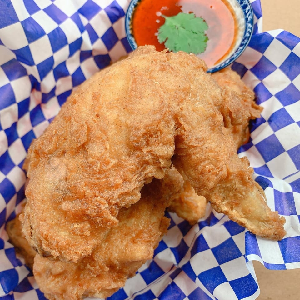 Crispy fried Thai chicken wings in a blue and white checkered basket with chili dipping sauce.