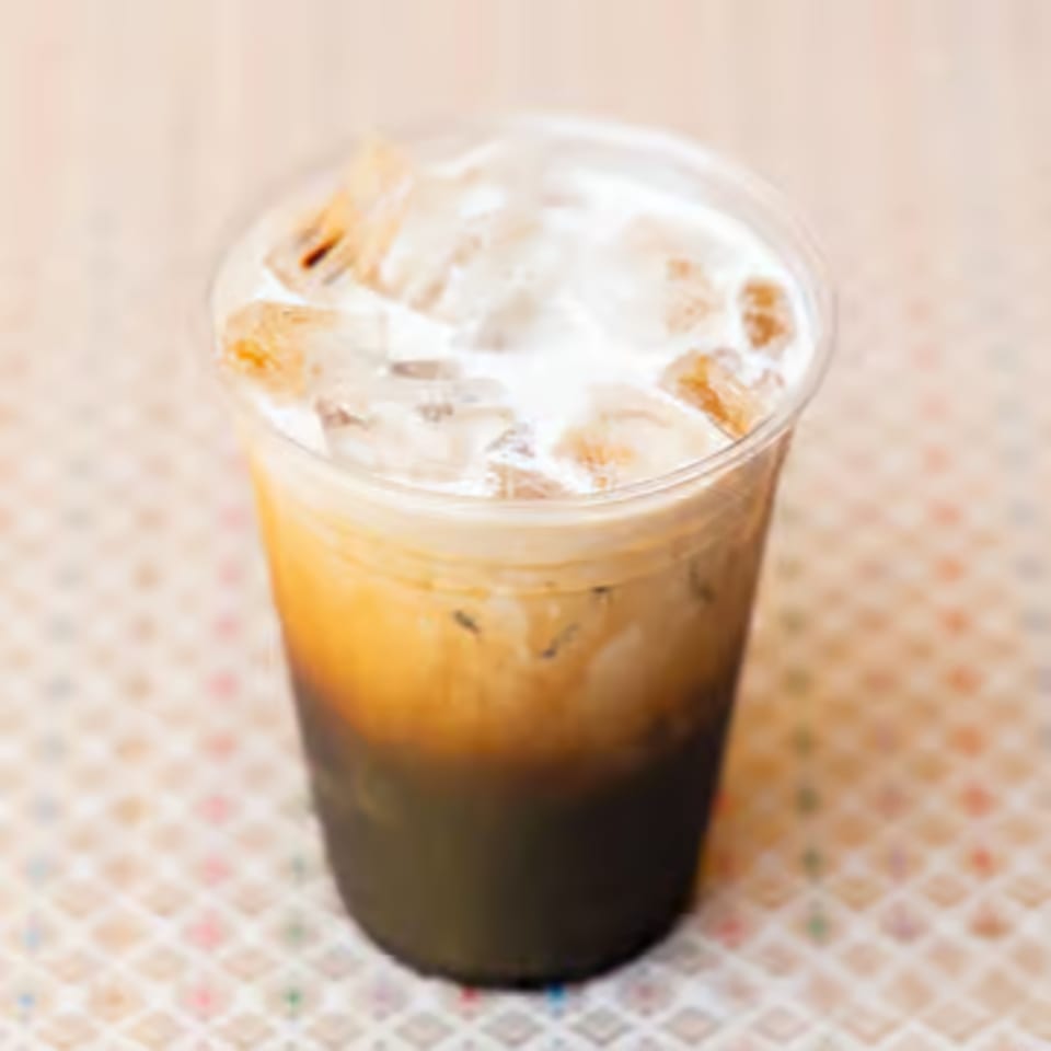 Iced Thai tea with milk and ice in a clear plastic cup on a patterned surface.
