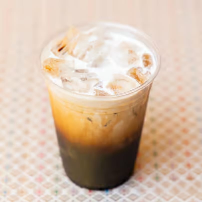 Iced Thai tea with milk and ice in a clear plastic cup on a patterned surface.