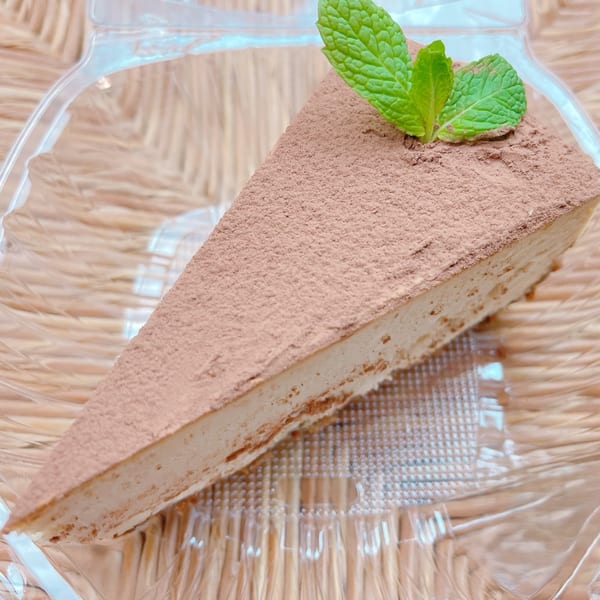 A slice of Thai tea cheesecake, dusted with cocoa powder and garnished with fresh mint leaves.